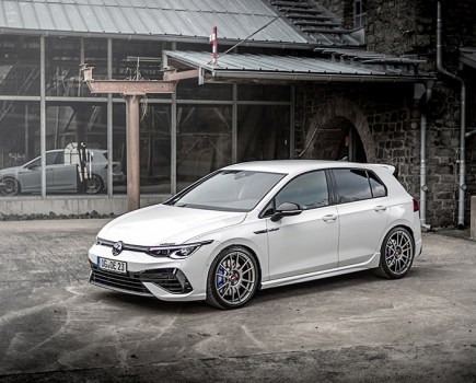 A front left shot of a white VW Golf Mk8 with modifications sat stationary next to glass with reflection
