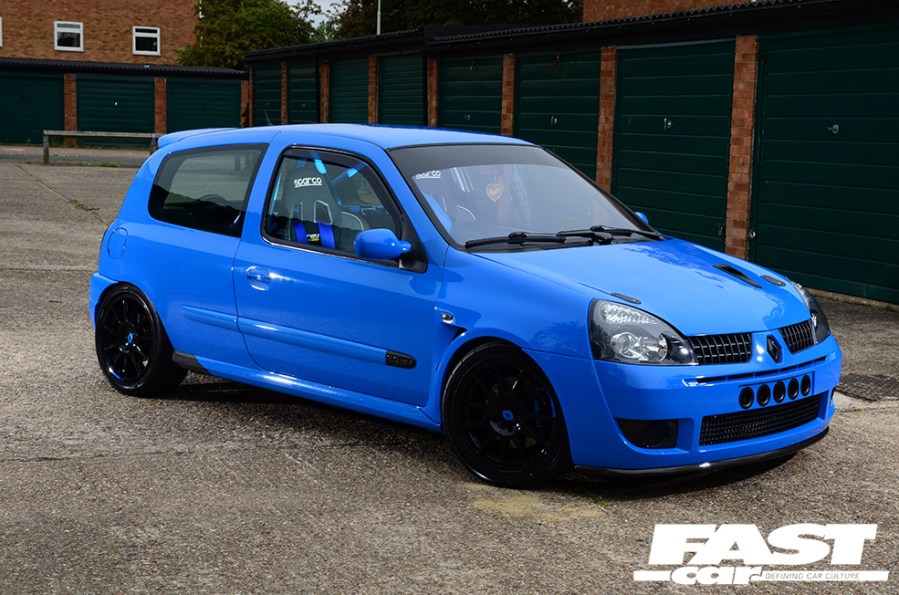A right side shot of a bright blue tuned Renault Clio 182 parked outside some residential garages