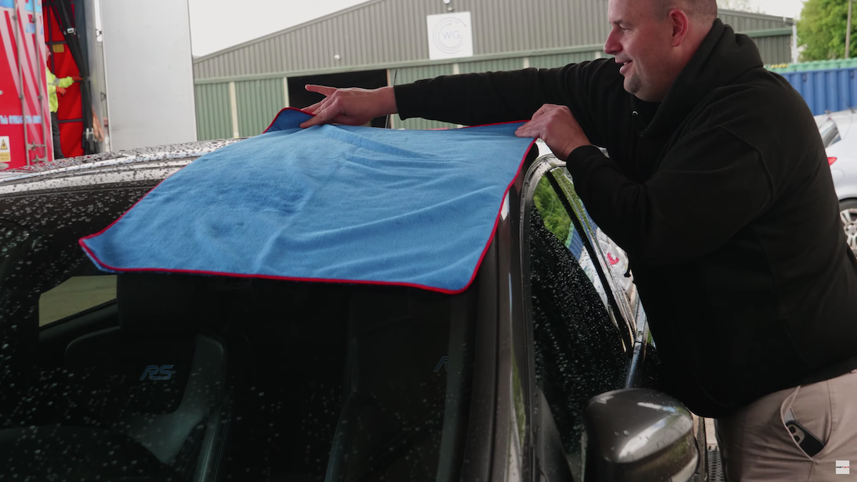 man using drying towel on roof of a car